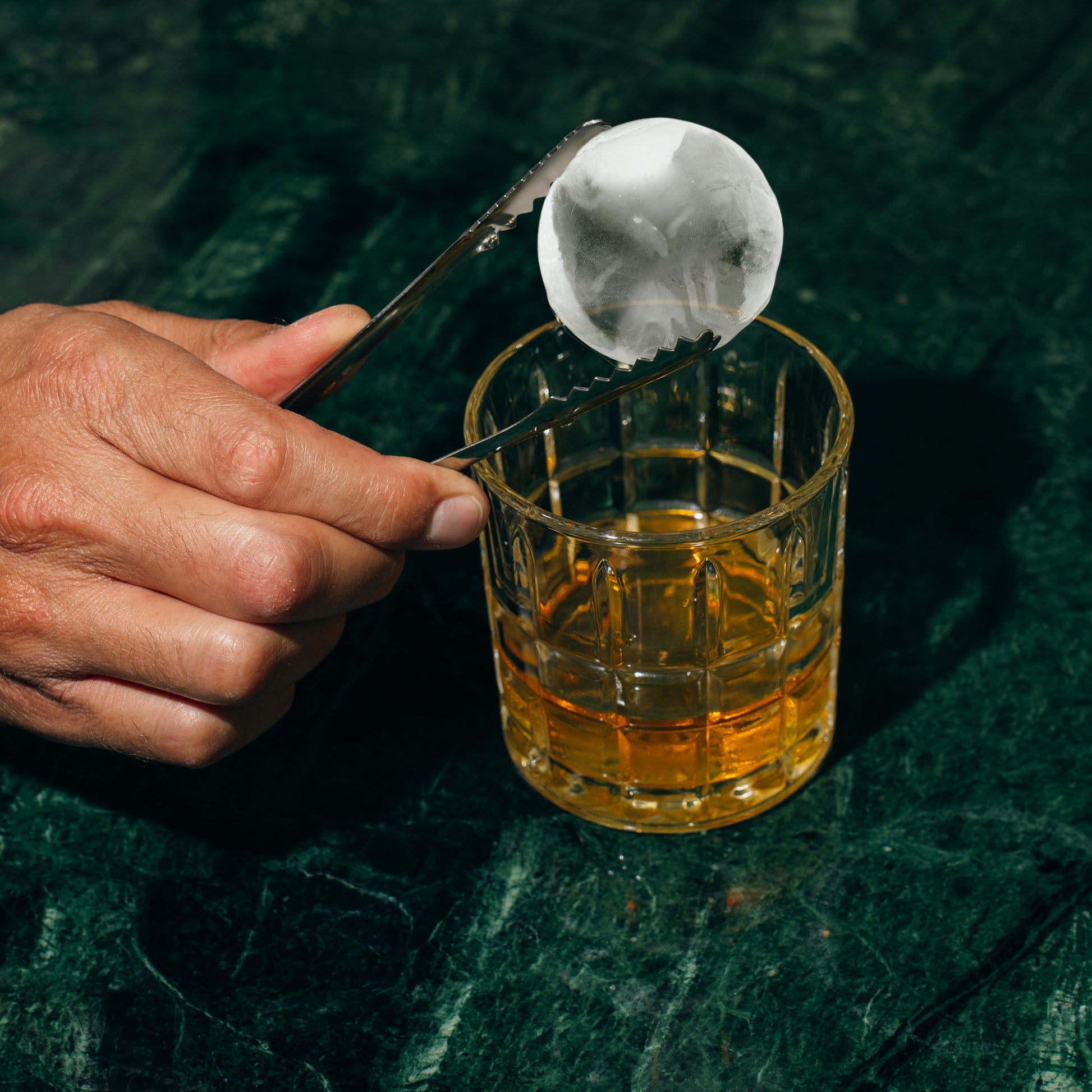 Ice ball next to a Whiskey Drink. 